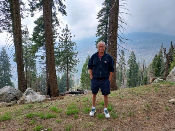 Photo of the author, a white-haired man, at Sequoia National Park in front of trees.