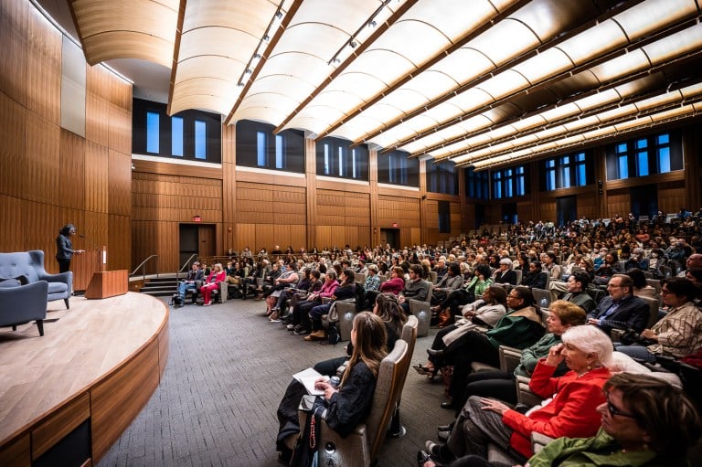 A person on a stage speaks to a packed auditorium