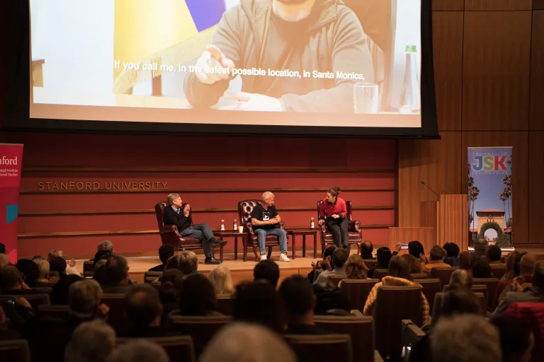 Three people sitting on the stage of an auditorium.