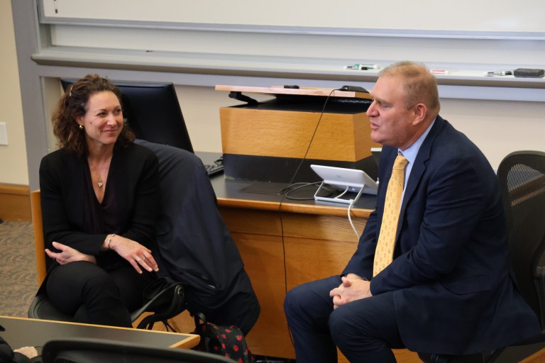 Two speakers sit across from each other at the front of a classroom.