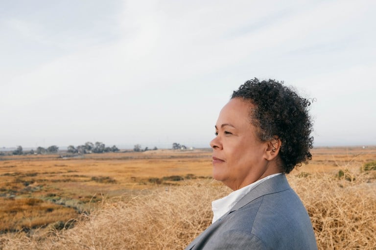 Julie Lythcott-Haims stares at a field with a trial in the background.