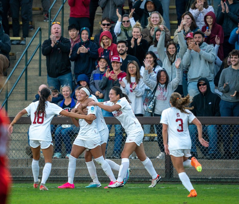 Players in the red and white Stanford uniform crowd under Maya Doms, who smiles towards the camera.