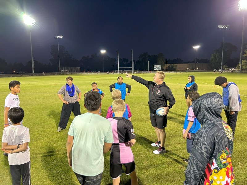 Richard Ashfield points across a rugby field, directly a group of local middle schoolers who are participating in the Reading & Rugby program.