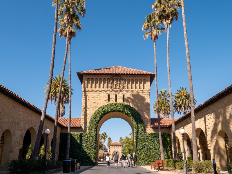 The arches of Main Quad, framed by rows of palm trees against a blue sky