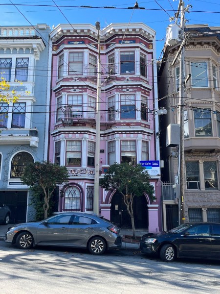 A picture of a tall pink house in the middle of a blue house, half in frame, and a brown house, half in frame.