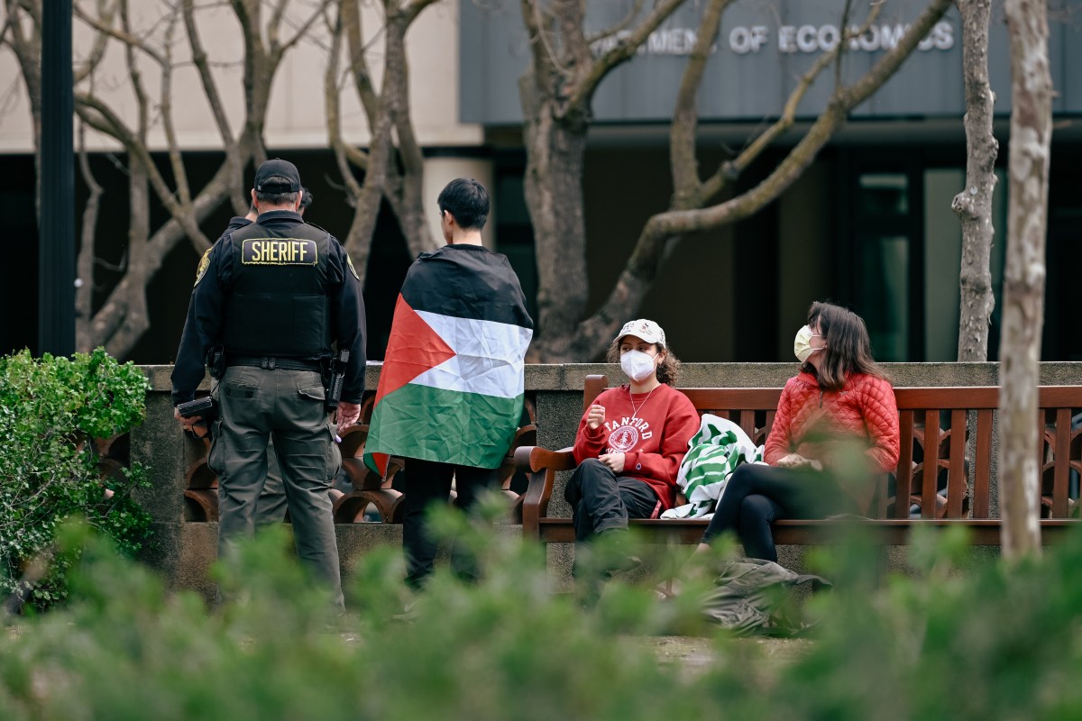 A sheriff stands next to a student with a Palestine flag wrapped around them. 