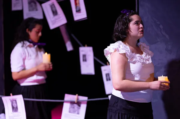 A young woman onstage holds a candle, looking into the distance. Behind her are 'missing' posters and another young woman holding a candle.