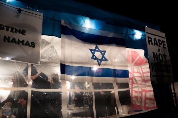 An Israeli flag hangs on a white tent with lights shining through.
