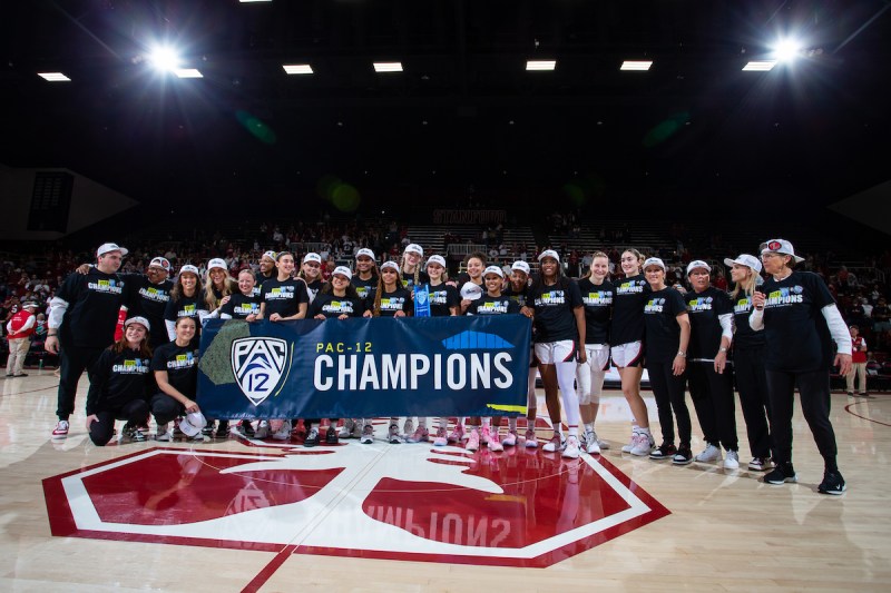 The women's basketball team holds a banner that reads champions and stands on the red Stanford S.