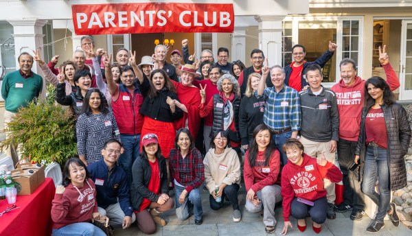 Members of the Stanford Parents Club posing, some of them are on on their knees, the rest are standing behind them, for a group picture with their hands in the air.