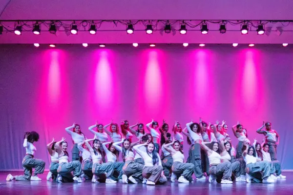 Stanford hip hop dance group 'Dv8' poses on stage at Dinkelspiel Auditorium. There are bright pink lights shining above them on stage.