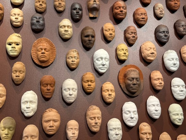 A wall featuring clay sculptures of human faces in varying colors. The sculptures are plaster casts of artist Ruth Asawa's friends and loved ones.