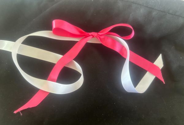 A tied pink ribbon with a white ribbon intertwined with it against a black background.