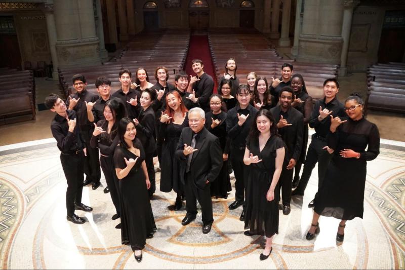 Stanford Chamber Chorale members stand with Stephen Sano, holding up the shaka, a common, friendly hand gesture used in Hawai'i.