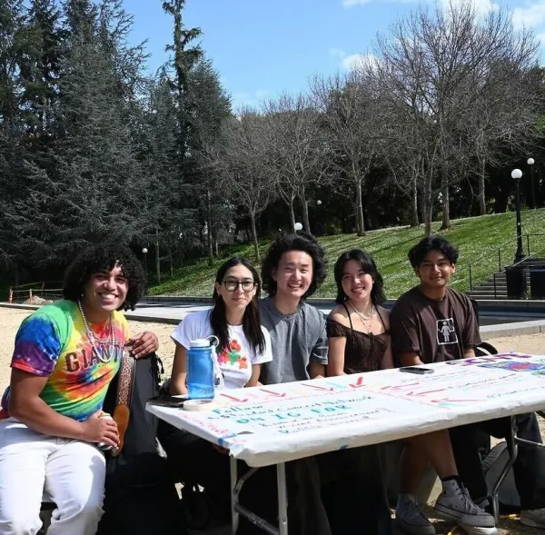 Members of the Stanford Concert Network sit behind a white table with posters on it in front of Terman Fountain.