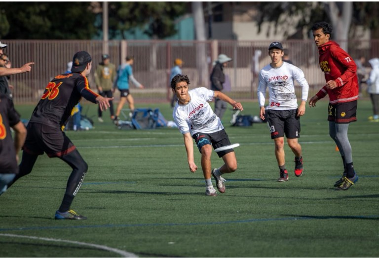 A Stanford ultimate frisbee player throwing a frisbee while other players run towards him.