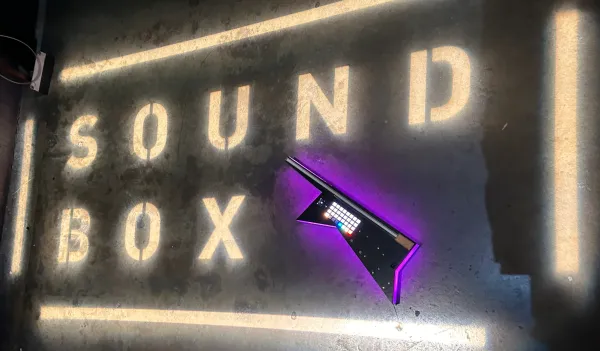 The Modulin is displayed in front of a sign reading "SoundBox" in white light-up letters.