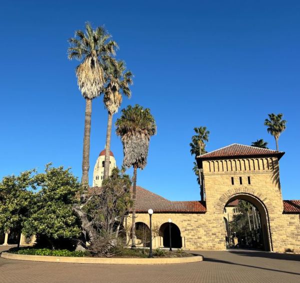 A photo of an archway in Main Quad with palm trees and Hoover Tower in the background.