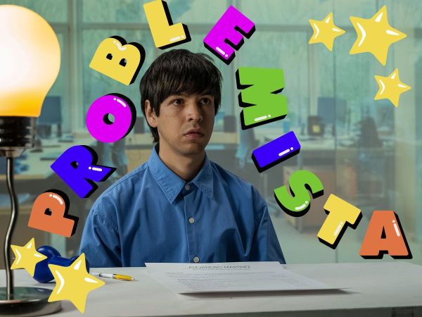 Julio Torres in the film Problemista, playing the role of aspiring toy designer Alejandro. Torres is wearing a blue collared shirt and is staring blankly ahead, and the film's title is displayed around him in colorful letters.
