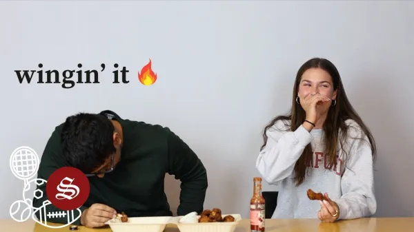 Elia Rubin laughs on camera as she eats a hot wing. A Stanford Daily sports editor next to her with Wingin' it and a fire emoticon written on the image.