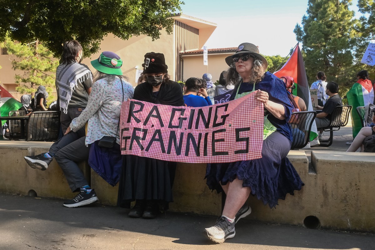 Two women hold up a banner that reads Raging Grannies with a red and white background.
