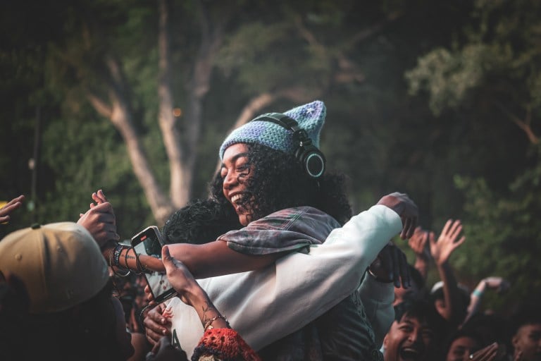 a woman wearing a crocheted cat ear hat smiles widely, embracing a fan in a full crowd