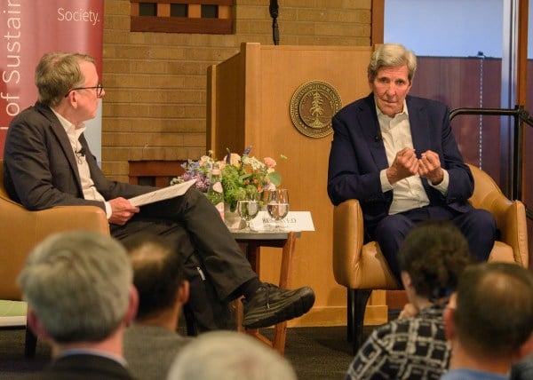 John Kerry sits across from a moderator on a stage.