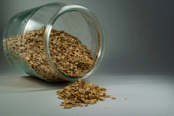 Brown oats in a clear glass jar against a gray background/wall.