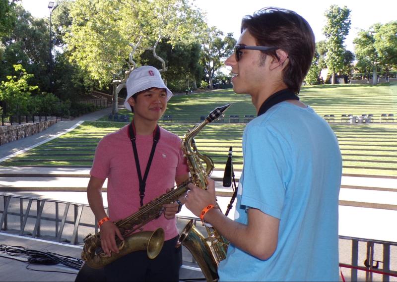 Saxophonists Quinn Simmons '27 and Ethan Htun '27 speak to each other on the stage of Frost Amphitheater, both holding saxophones.