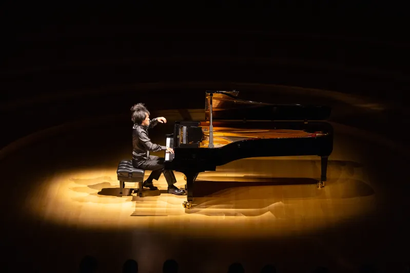 Bruce Liu, head bowed, plays a grand piano under a dramatic spotlight