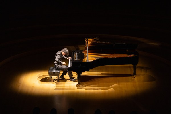 Bruce Liu, head bowed, plays a grand piano under a dramatic spotlight