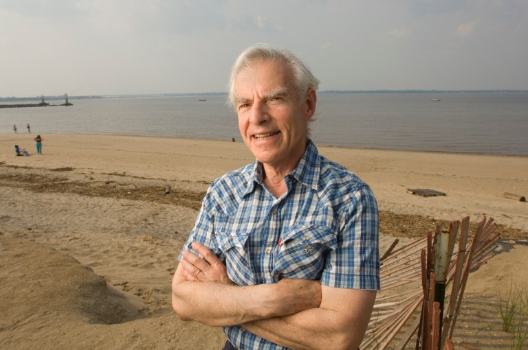 Howard Bruce Franklin, age 73, stands in front of a beach on a cloudy day.