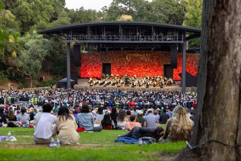 Crowds of students and audience members are seated at Frost Amphitheater watching the San Francisco Symphony perform.