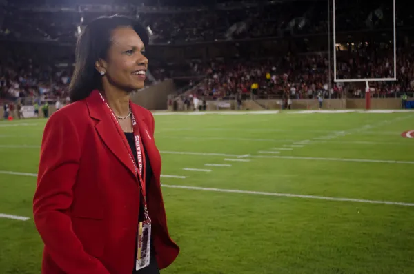 Condoleezza Rice stands smiling on the field of a Stanford football game.