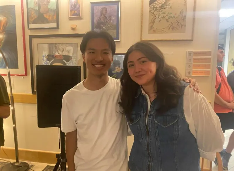 Ben Yan '25 MS '26 is standing next to Kathaleen Mallard '25 in front of a wall with many framed pictures. (Photo: JUDY LIU/The Stanford Daily)