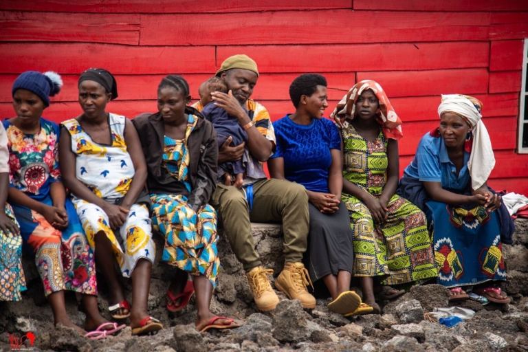 A group of Congolese people sit side-by-side in front of a red wall.