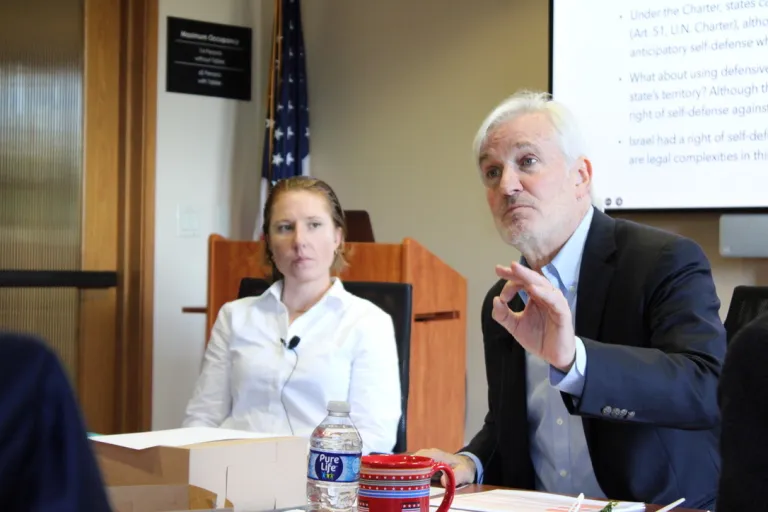 Law professor Allen Weiner speaks while gesturing. Behind him, an attendee watches him speak.