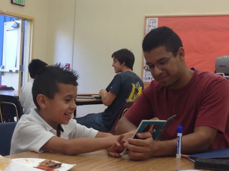 A tutor and a young kid are reading a book together.