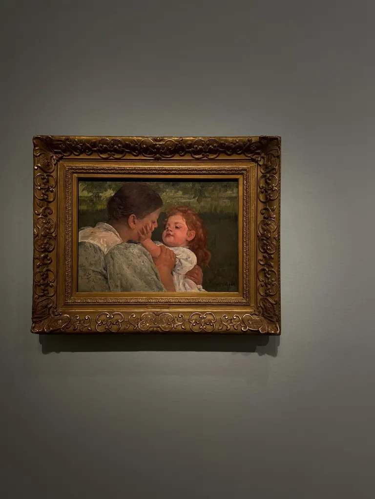 Photo taken of "Maternal Caress" which paints a tender moment between a woman and a young child set against a natural green background.