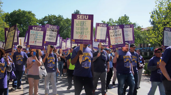 Striking SEIU members hold up purple signs.