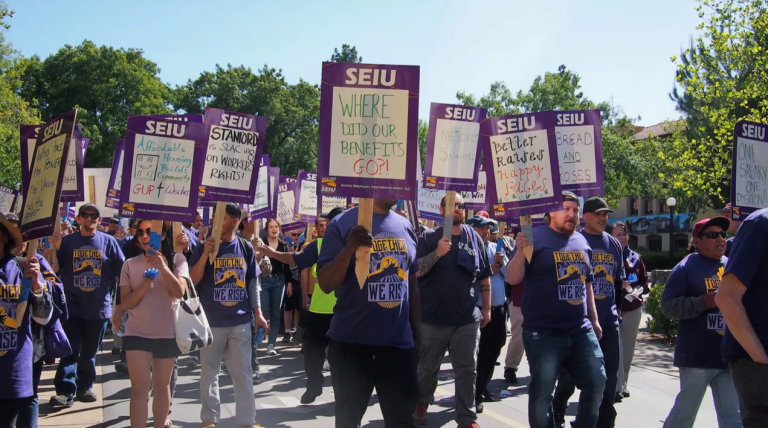 Striking SEIU members hold up purple signs.