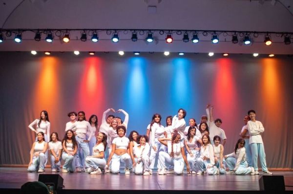 Picture of the dance group Legacy on stage, posing all together as a group after their set; some are squatting and some are standing.