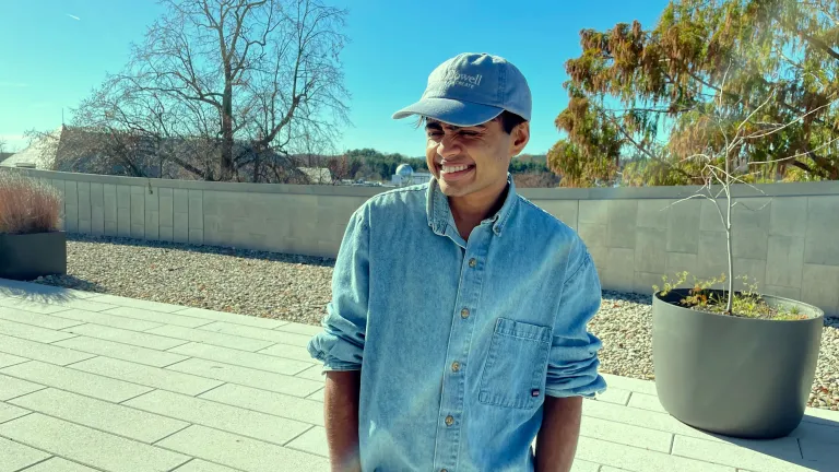 Headshot of Janani Balasubramanian; they are wearing a blue shirt and matching blue hat and turning slightly to the left, smiling.