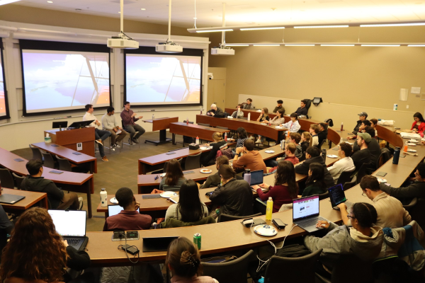 Lecture room where people are sitting in rows of desk facing a projector