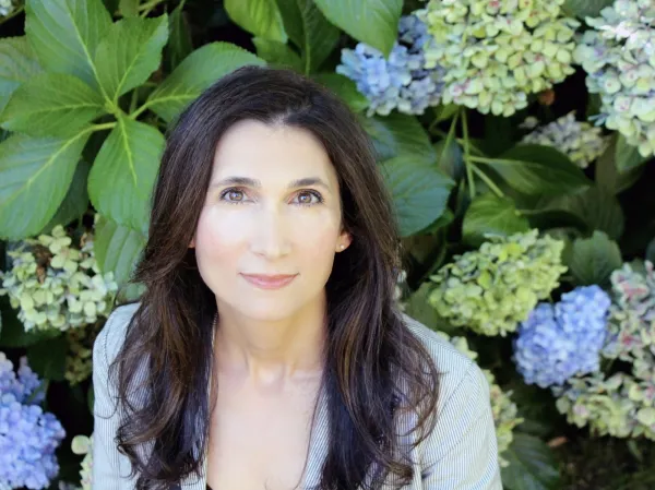 Diana Farid gazes at camera against in front of green leaves and light blue/green hydrangeas.