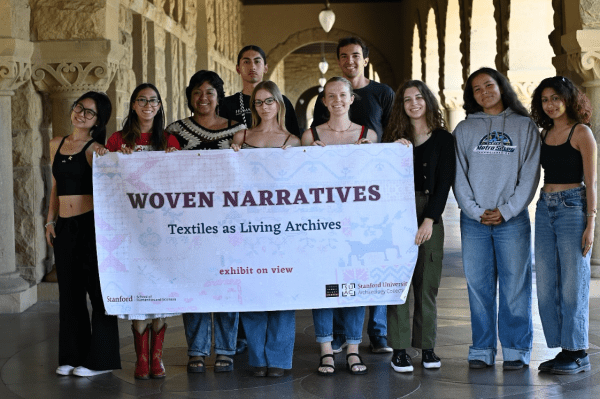Students stand in Main Quad arches with a poster in the middle of them.