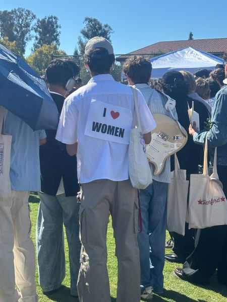 a man stands with his back to the camera. the back of his shirt reads "I heart women"
