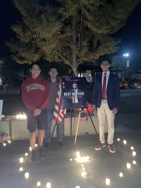 Organizers stand beside a photo of Charlie Kirk at a nighttime vigil.