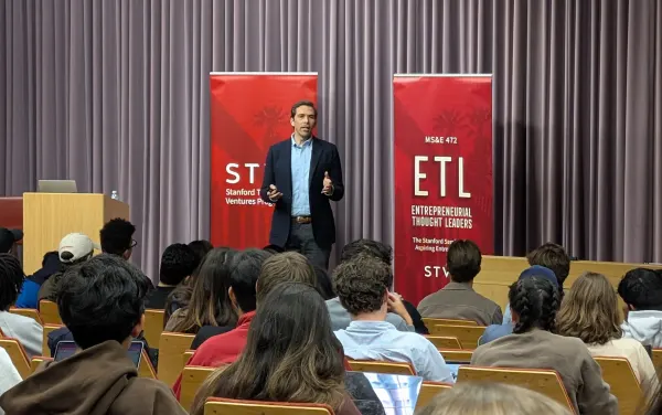 Eric Volmar speaking at the front of a lecture hall.