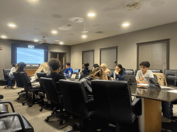 The UGS sitting around a table listening to a presentation on a screen